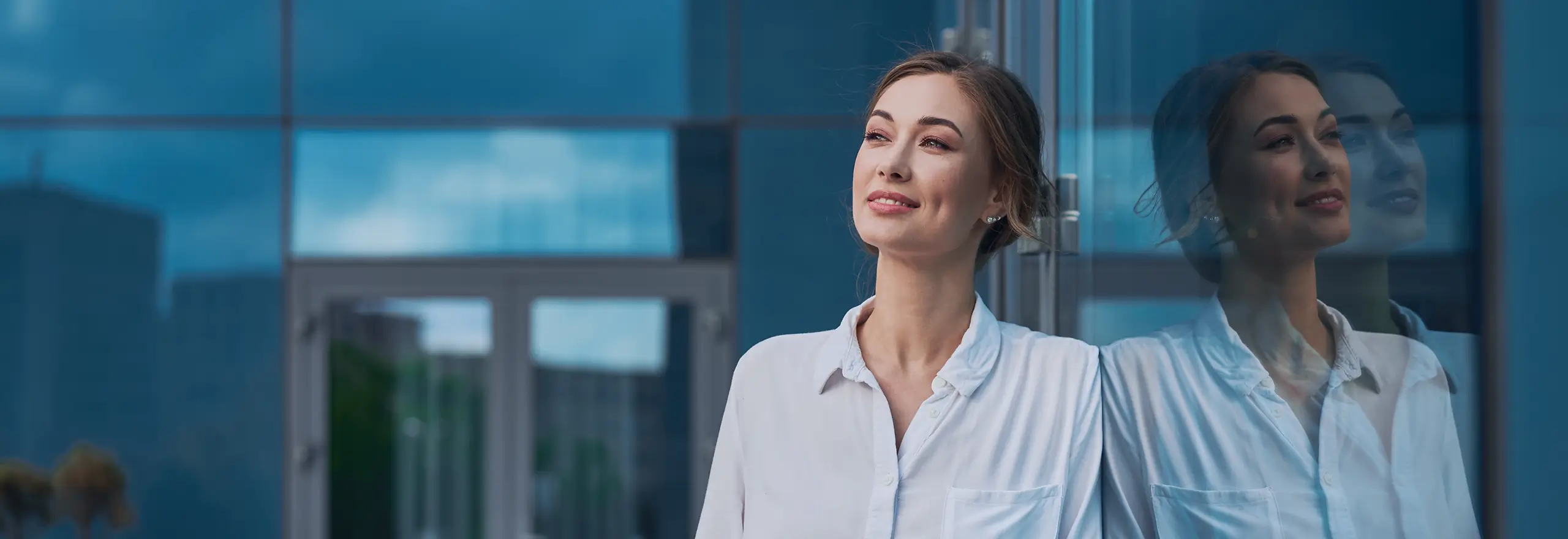 Mulher com expressão confiante e serena refletida no vidro de um prédio corporativo — representando autoconhecimento, crescimento pessoal e o olhar para o futuro que a Volare promove em suas consultorias e mentorias individuais.