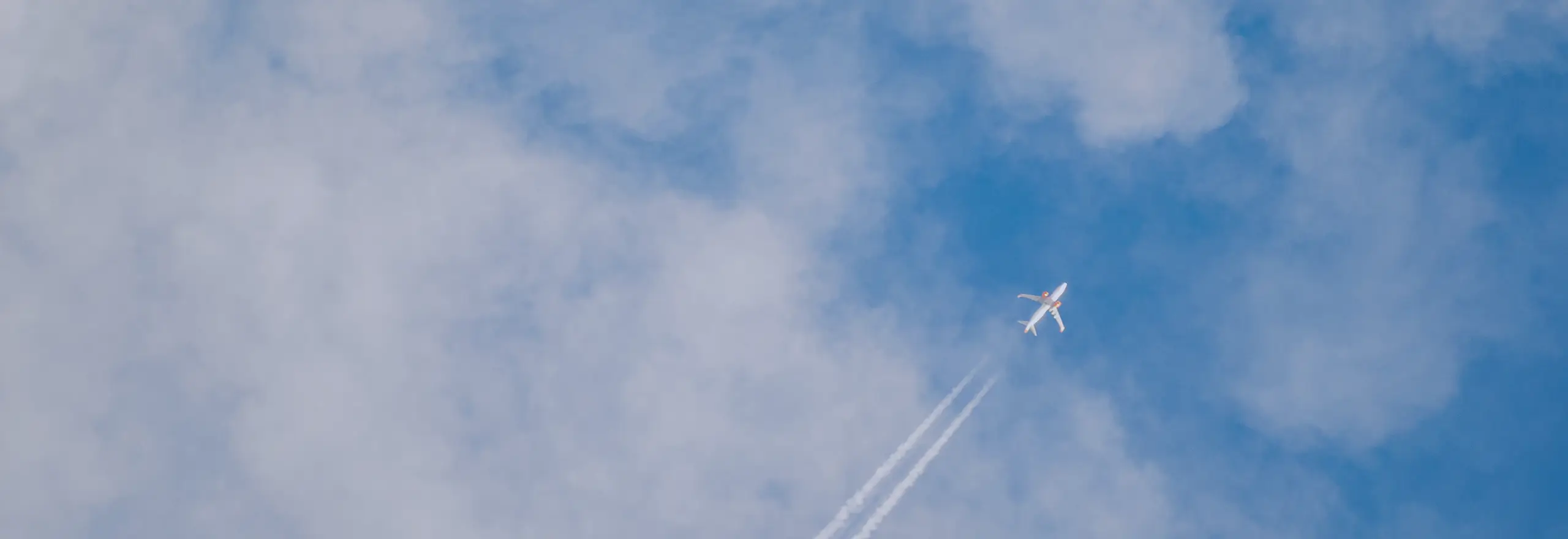 Avião em ascensão cruzando o céu com trilhas brancas entre as nuvens — simbolizando trajetória, evolução e a missão da Volare de impulsionar pessoas e organizações rumo a novos voos.